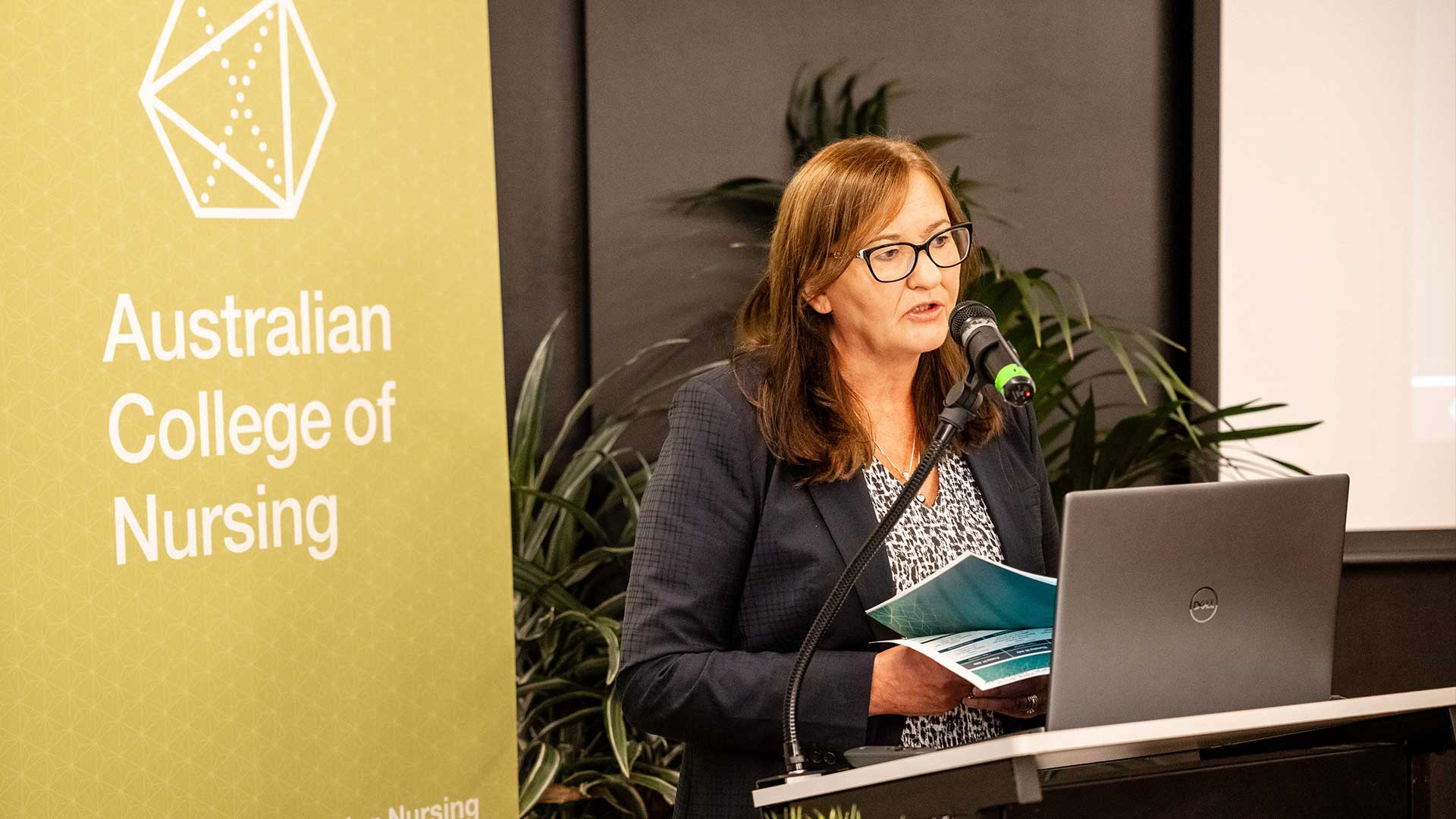 Woman standing at lecturn speaking in front of a microphone