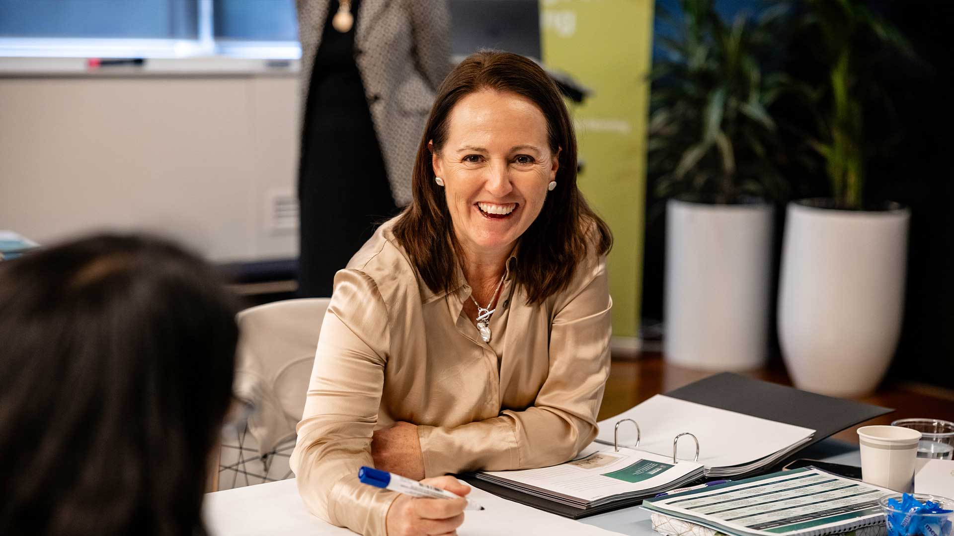 Woman sitting at a desk with pen in hand smiling at the camera